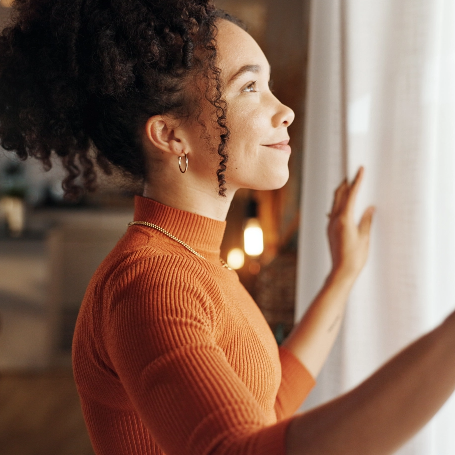 Ragazza che guarda dalla finestra senza occhiali, serenità dopo visita oculistica ADVALIA a Milano